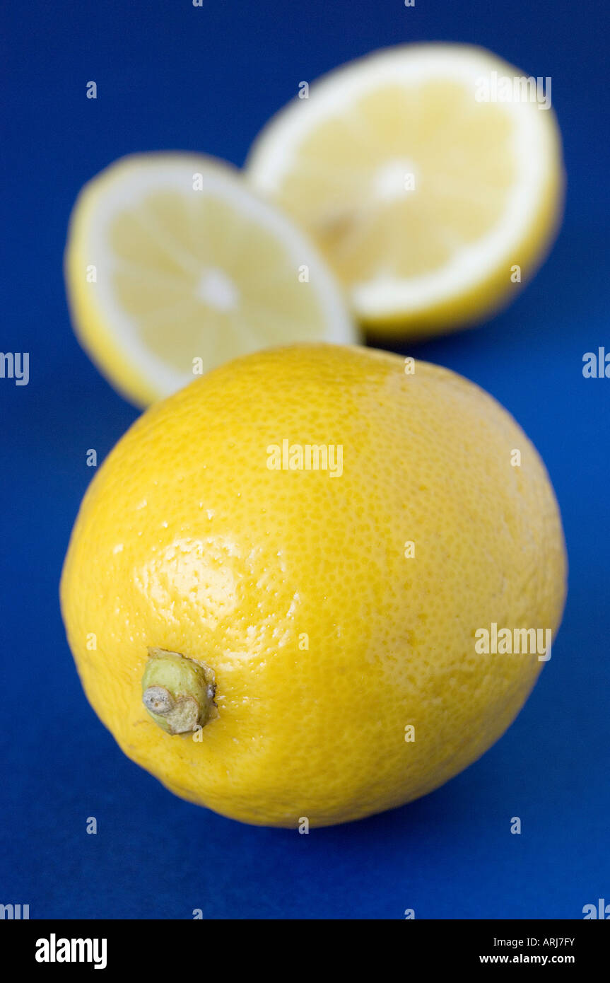 Eine ganze frische Bio-Zitrone mit einem defokussierten, geschnittenem Obst im Hintergrund gegen blau Stockfoto