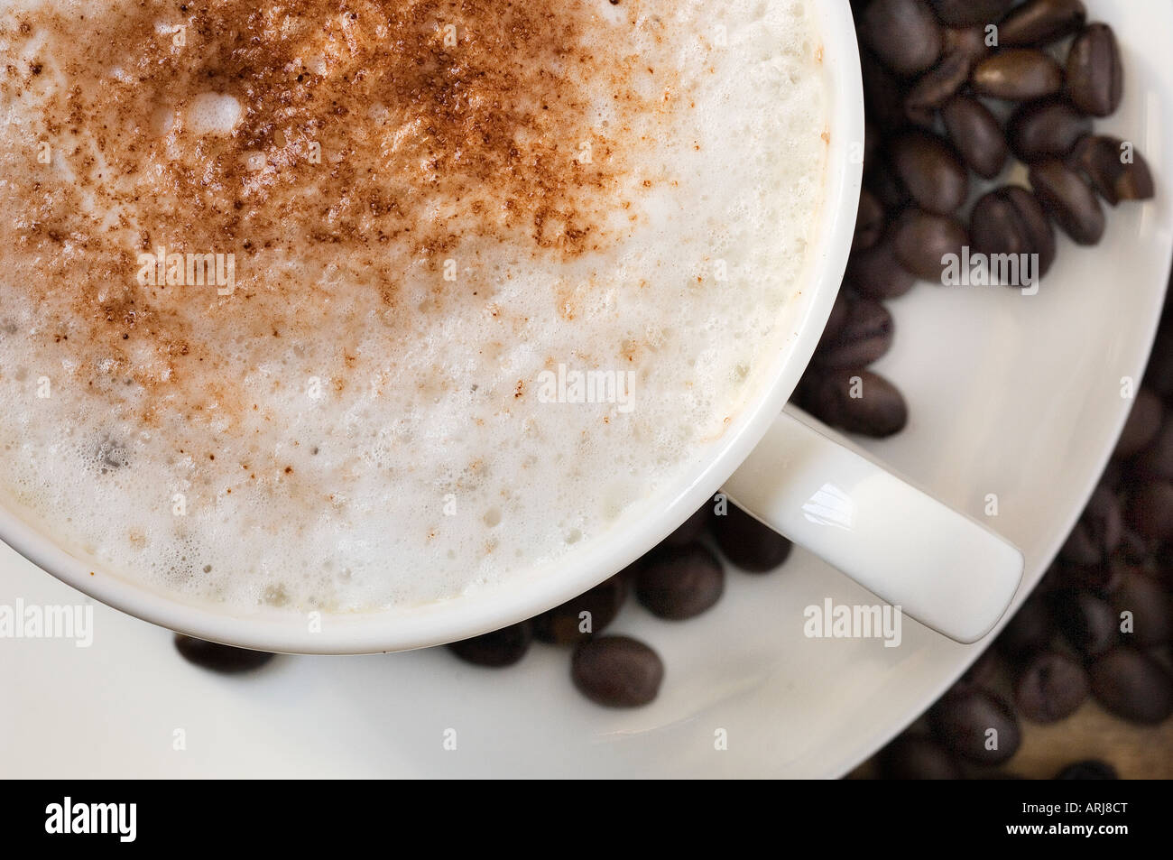Eine Nahaufnahme von frisch zubereiteten Cappuccino Tasse auf eine Untertasse, umgeben von gerösteten Kaffeebohnen Stockfoto