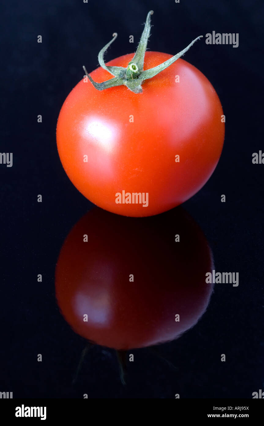 Ein frisches Bio Tomaten mit seinen Stiel befestigt auf einem schwarzen reflektierenden Hintergrund Stockfoto