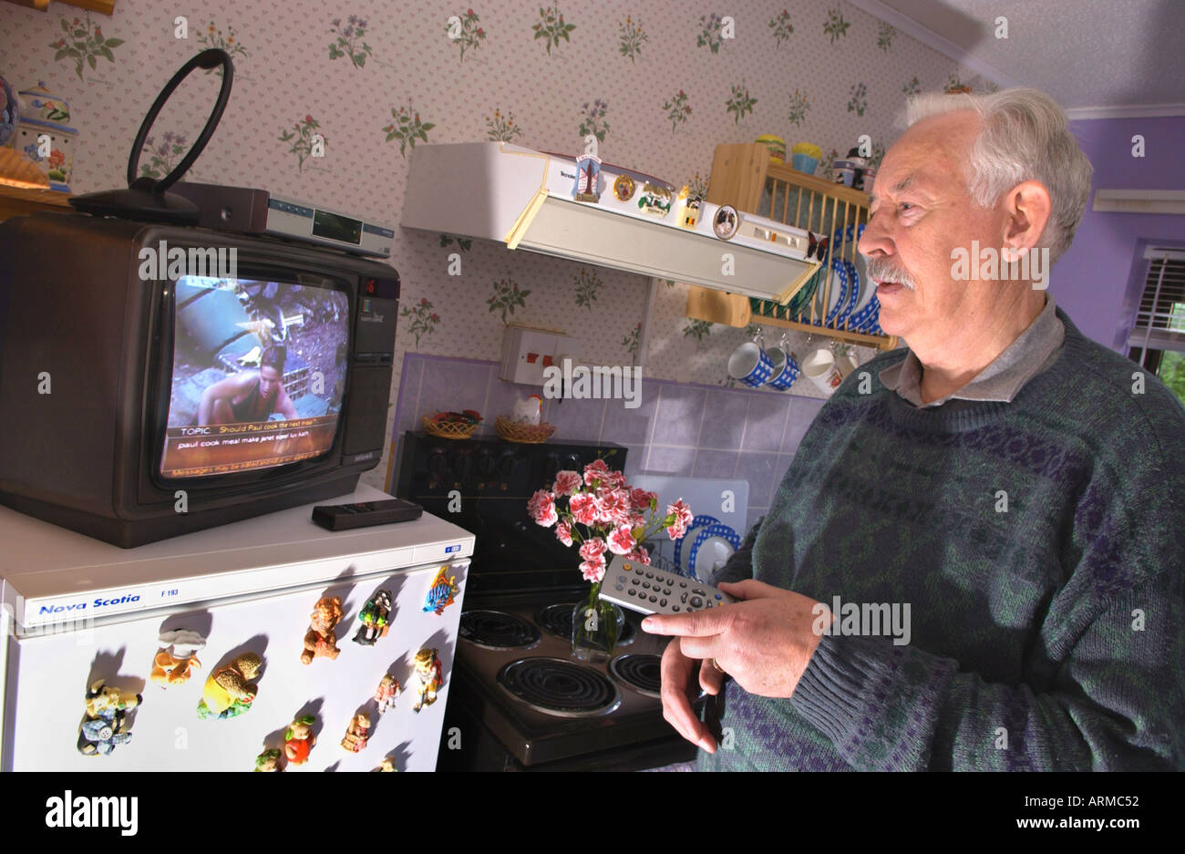 Älterer Mann mit seinem Fernsehen digitale Set-Top-Box in der Küche des Hauses im Dorf von Ferryside Carmartheshire West Wales UK Stockfoto