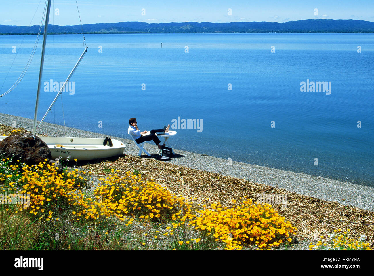 Mann mit tragbaren Tisch, Stuhl, Computer und Handy in outdoor-Büro am Clear Lake, Calilfornia Stockfoto