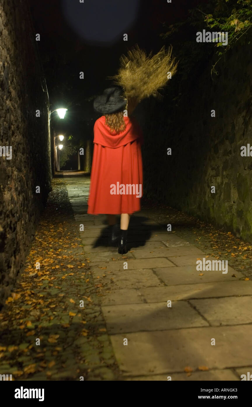 Hinten Wiew einer jungen Frau trägt einen roten Umhang und Hexe Hut nachts in einer einsamen Gasse Stockfoto