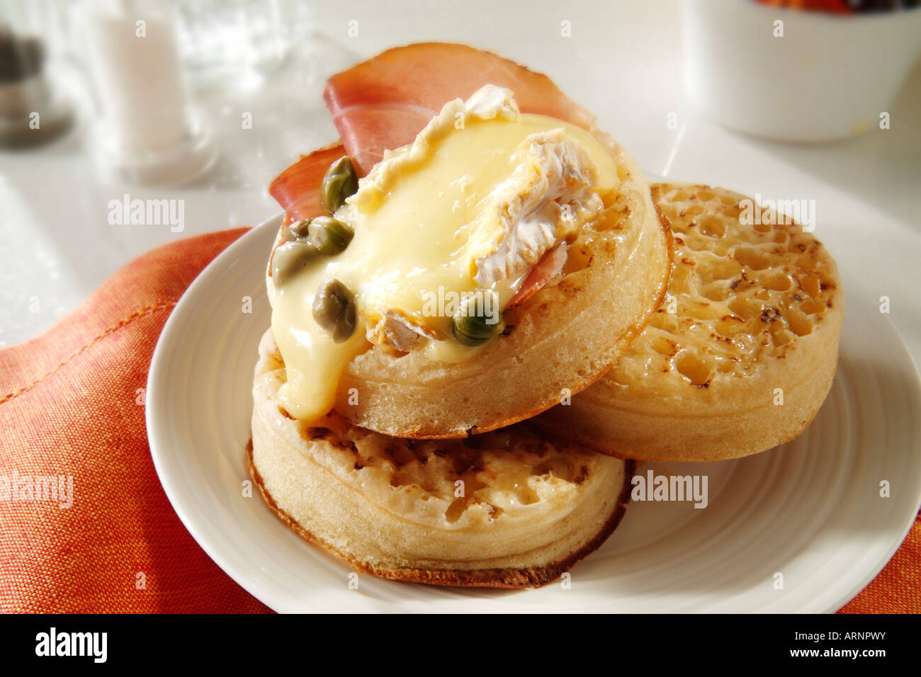 Hot ausgesprochen Crumpets mit geschmolzenem gegrillte Brie oder Camembert oder Ziegen Käse und Kapern, auf einem weißen Teller in einer Tabelle serviert. Stockfoto