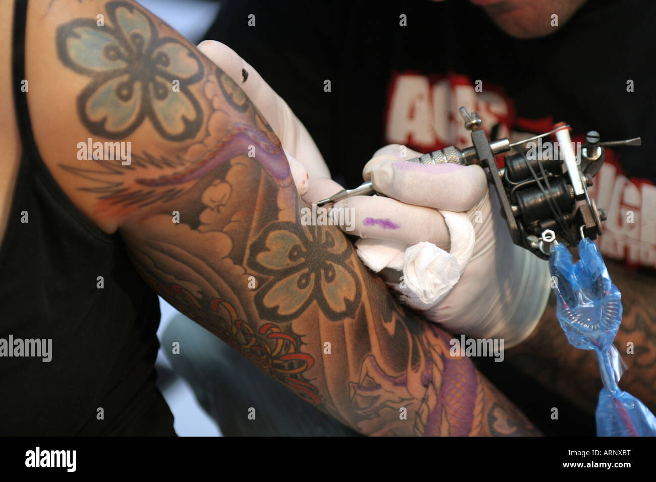 Ein Tattoo-Künstler kennzeichnet den Arm eines Kunden durch Einfügen von Pigment in der Haut die Kunst der Tätowierung zurück mindestens 5000 Jahre Stockfoto