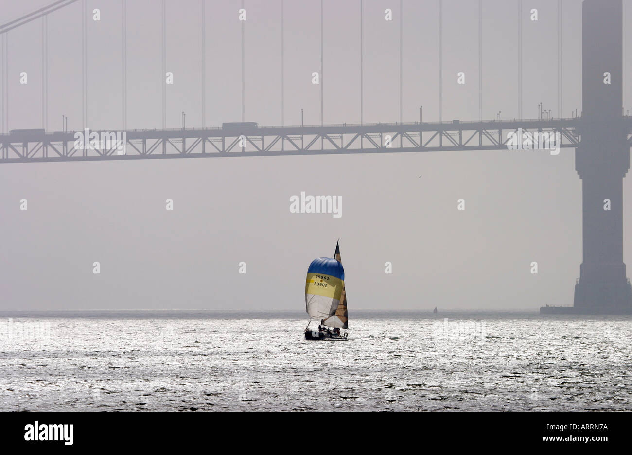 eine einsame Yacht segelt in die Bucht von San Francisco mit der Hintergrundbeleuchtung Golden Gate-Brücke in der Ferne Stockfoto
