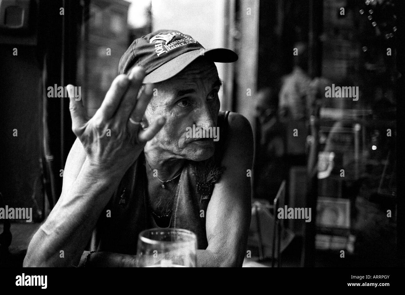 Älterer Mann im Pub, gestikulieren mit einer Hand während des Sprechens mit jemandem aus dem Rahmen. Stockfoto