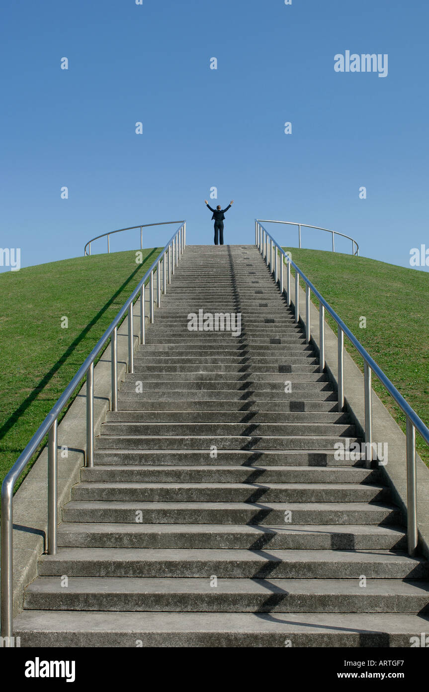 Person mit den Armen in der Luft an der Spitze der langen Treppe bergauf Stockfoto