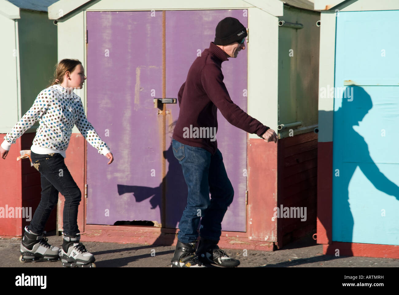 Ein junges Mädchen Schlittschuhe mit einem Mann vorbei Strandhütten in Hove in der Nähe von Brighton England UK Stockfoto