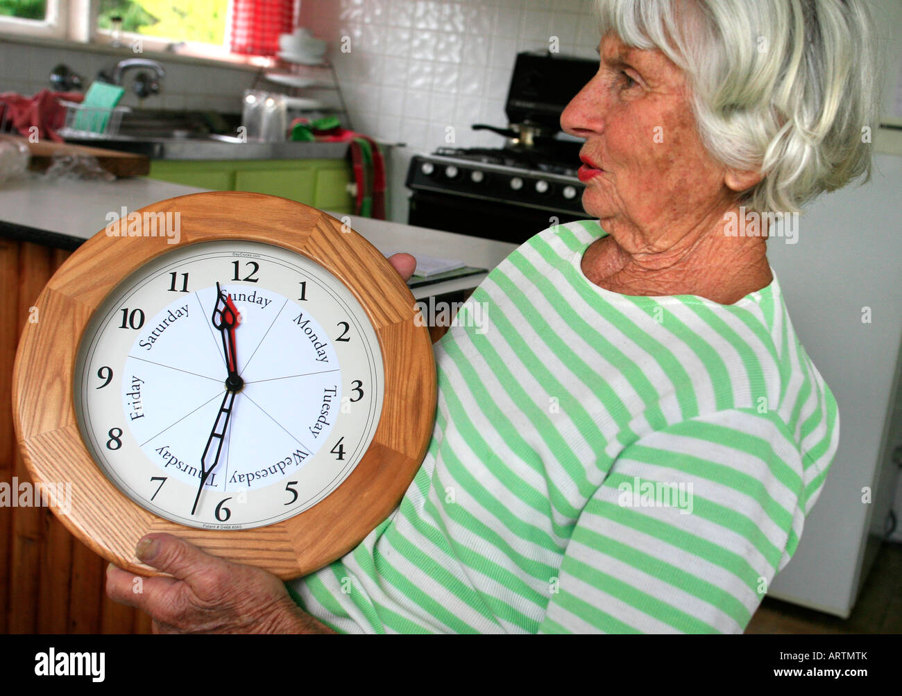 Eine ältere Frau mit einigen Gedächtnisverlust hält eine Uhr, die den Wochentag und die Uhrzeit anzeigt Stockfoto