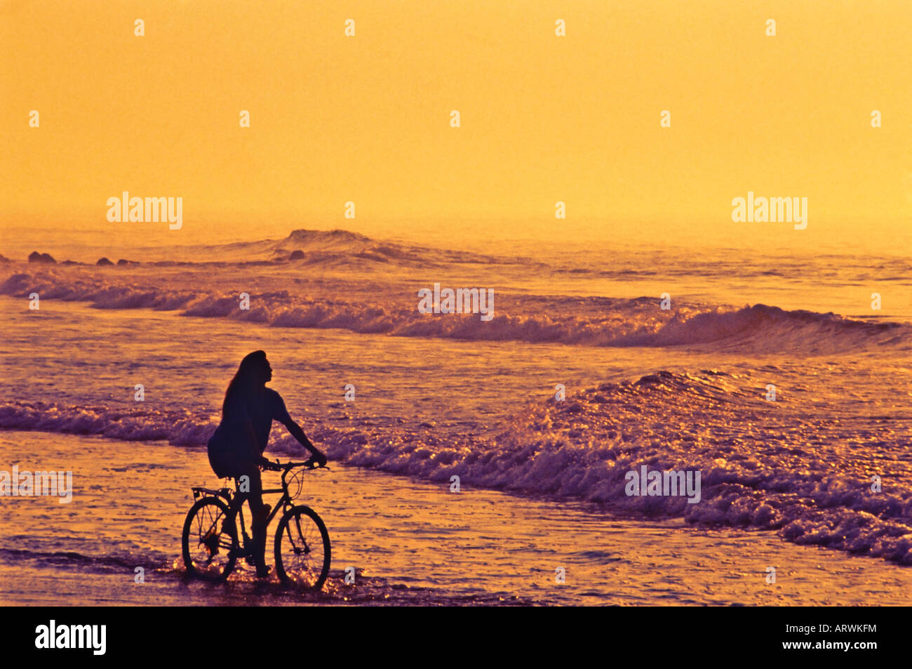 Frau Reiten Fahrrad am Strand bei Sonnenuntergang Stockfoto