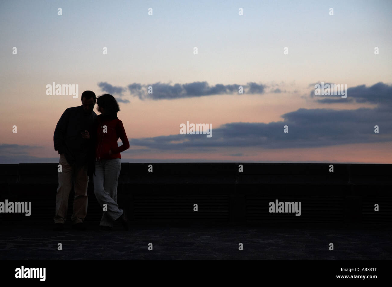 paar in der Silhouette, ein Handy zu betrachten, wenn die Sonne Behing konkrete untergeht Wand-Santa Cruz-Teneriffa-Kanarische Inseln-Spanien Stockfoto