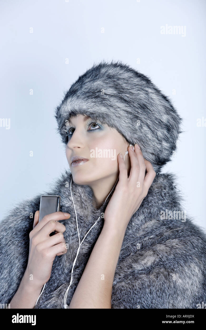 Studio shot Porträt einer schönen Frau russische Art in einem Pelzmantel und Hut Schuss Studioportrait von einer schönen Frau russischen Typs in einem Pelzmantel und Hut mit ihren Multimedia-Player Musik hören Stockfoto