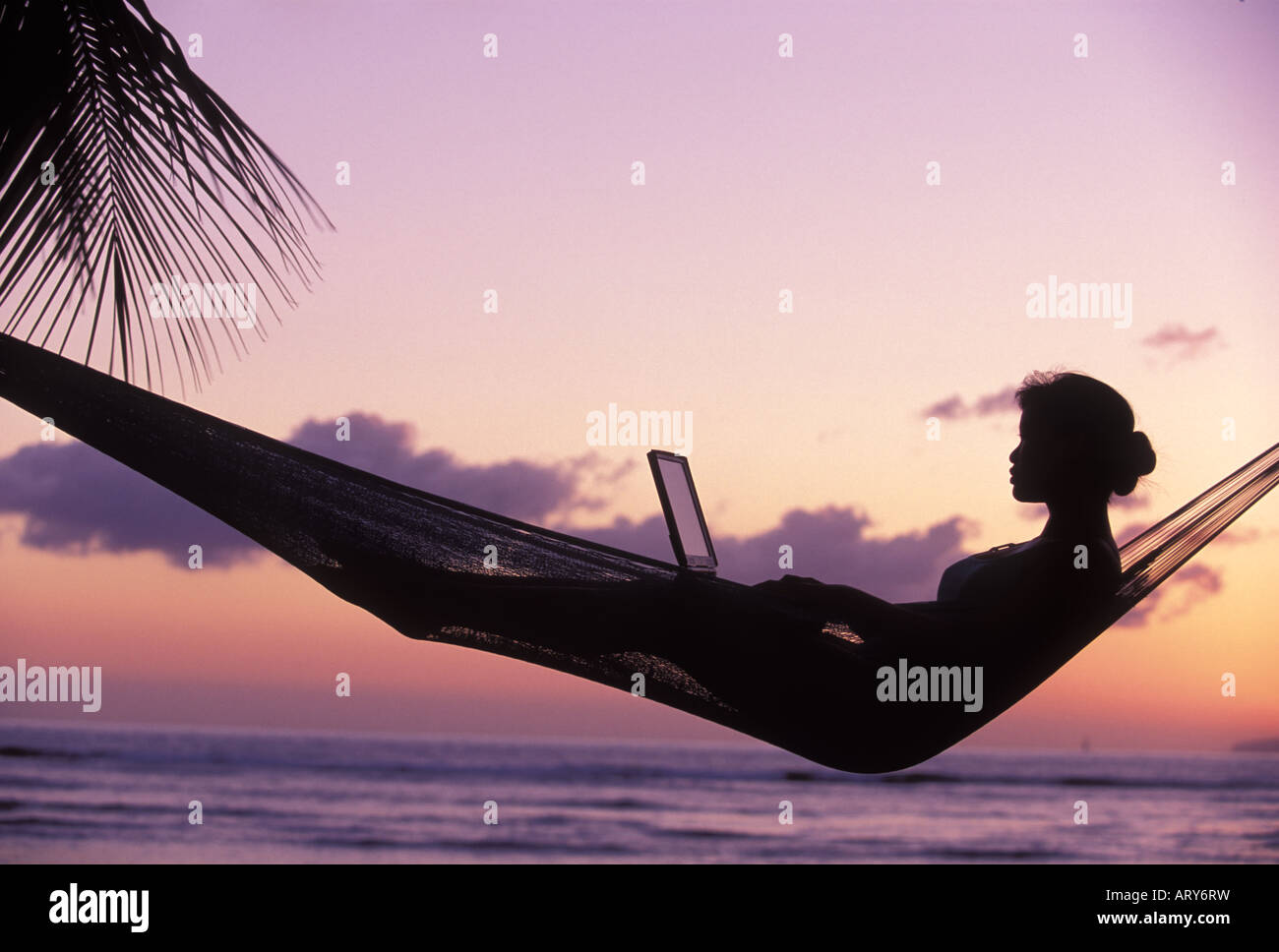 Eine Frau in einer Hängematte benutzt einen Laptop auf einer West Maui Sunset. Stockfoto