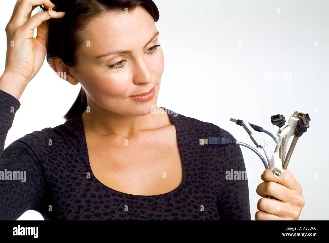 Frau, die kratzen, ihr Kopf auf der Suche auf ein Bündel von Computerkabel, verwirrt Stockfoto