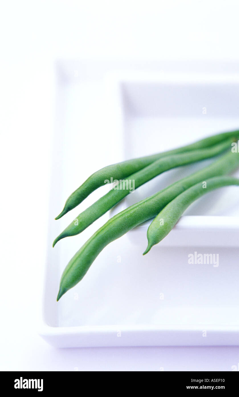 Grüne frische Bohnen aufreizend über eine Reihe von quadratischen Platten hängen wie eine Hand auf sauberen, weißen Hintergrund Stockfoto