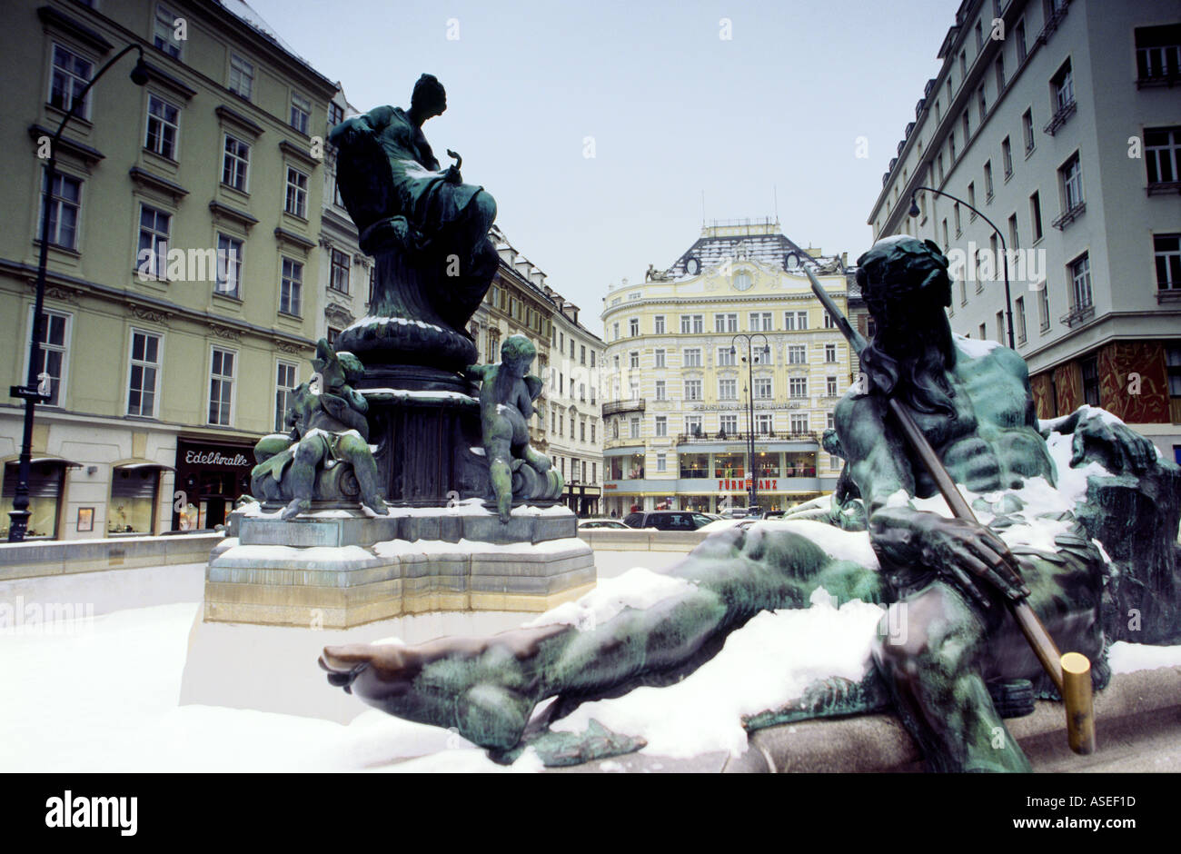 Zwei oxidierte Bronzestatuen von einem Brunnen umgeben von alten grand shopping Covered im Schnee im Winter Stadt Zentrum Wien Aust Stockfoto