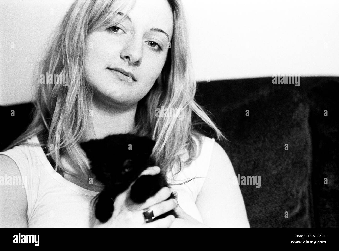 Junge Frau mit blonden schulterlangen Haaren neigt ihren Kopf und schaut der Betrachter halten Sie ein kleines schwarzes Kätzchen. Stockfoto