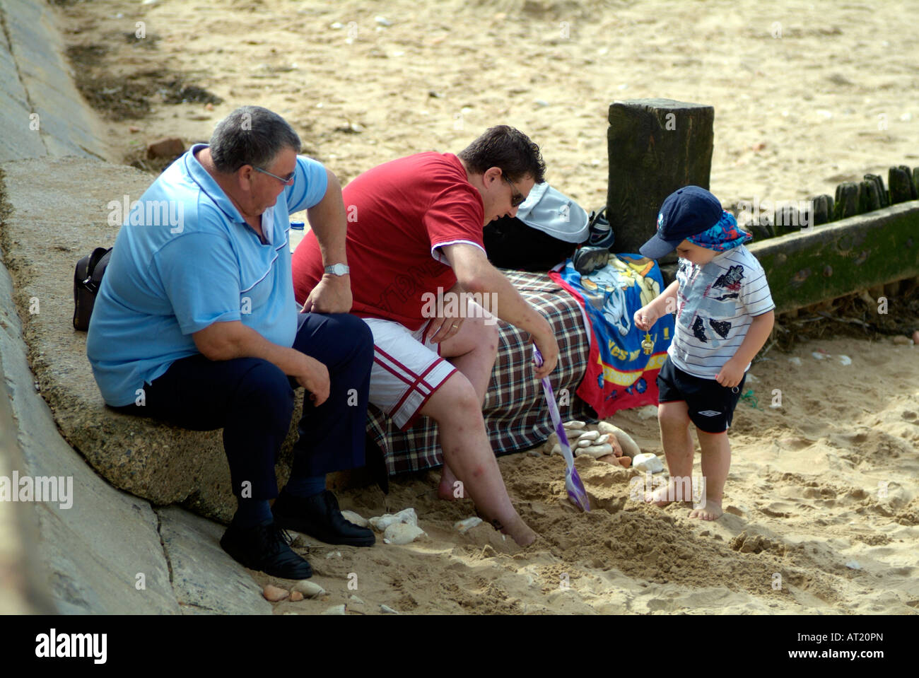 Übergewichtige Männer spielen am Sandstrand mit kleinen Jungen Stockfoto