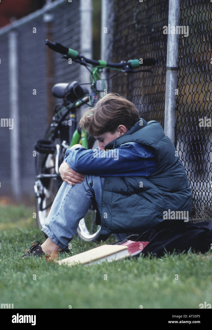 Deprimiert gemobbt, einsame Teen boy sitting gegen Maschendrahtzaun Stockfoto