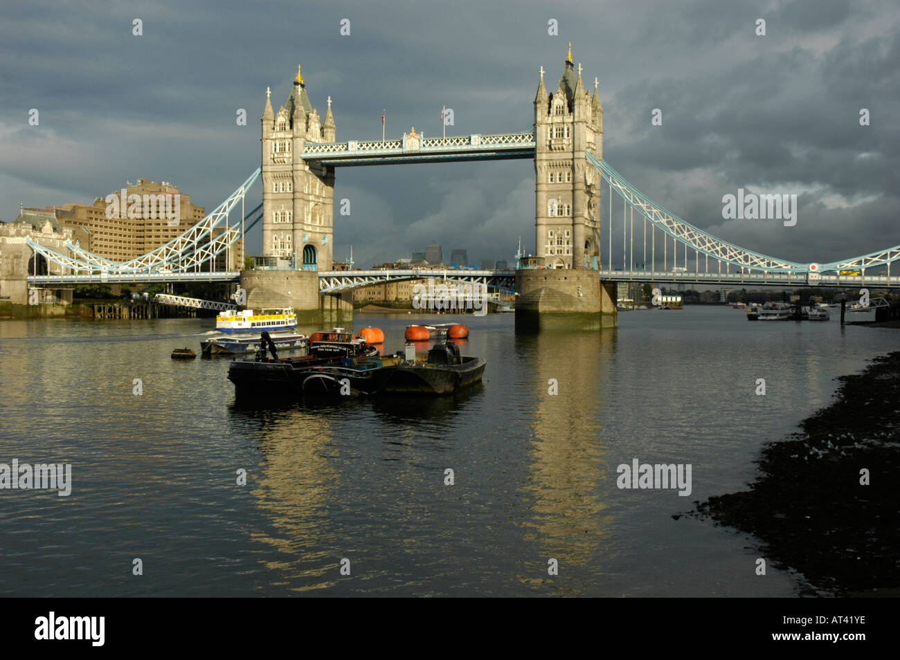 Fernblick über die Tower Bridge und Vordergrund Boote sonnenbeschienenen gegen ominösen dunklen grauen Himmel London UK Stockfoto