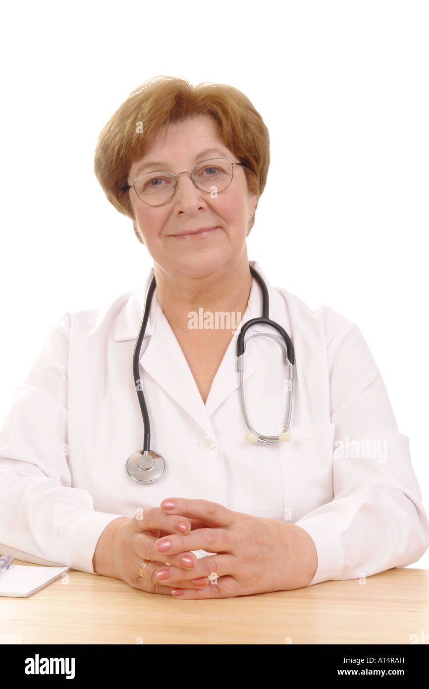 Porträt der freundliche senior Hausarzt mit Stethoskop sitzt hinter einem Schreibtisch auf weißem Hintergrund Stockfoto