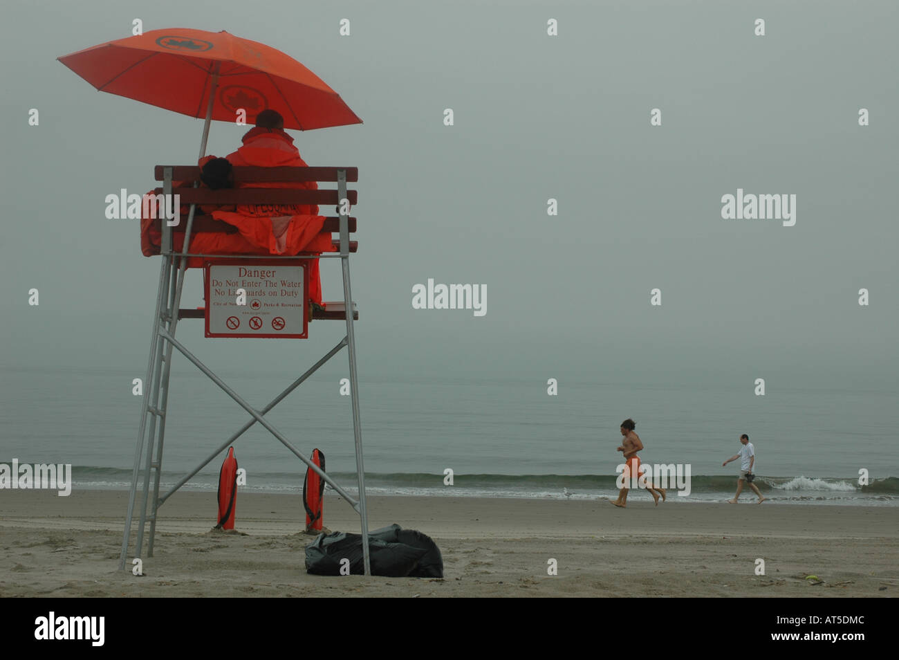 Rettungsschwimmer während einem Nieselregen regnerischen Tag mit einem Jogger in Strand von Coney Island auf Rettungsschwimmer Stuhl sitzend Stockfoto