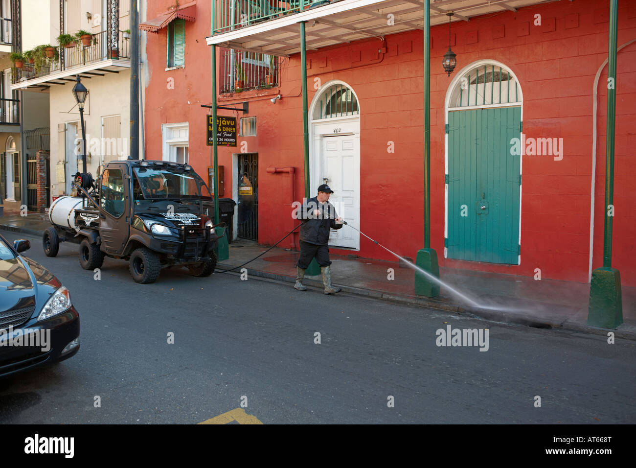 Ein Mann wäscht den Bürgersteig mit einem Hochdruckschlauch im historischen French Quarter von New Orleans, Louisiana, USA. Stockfoto