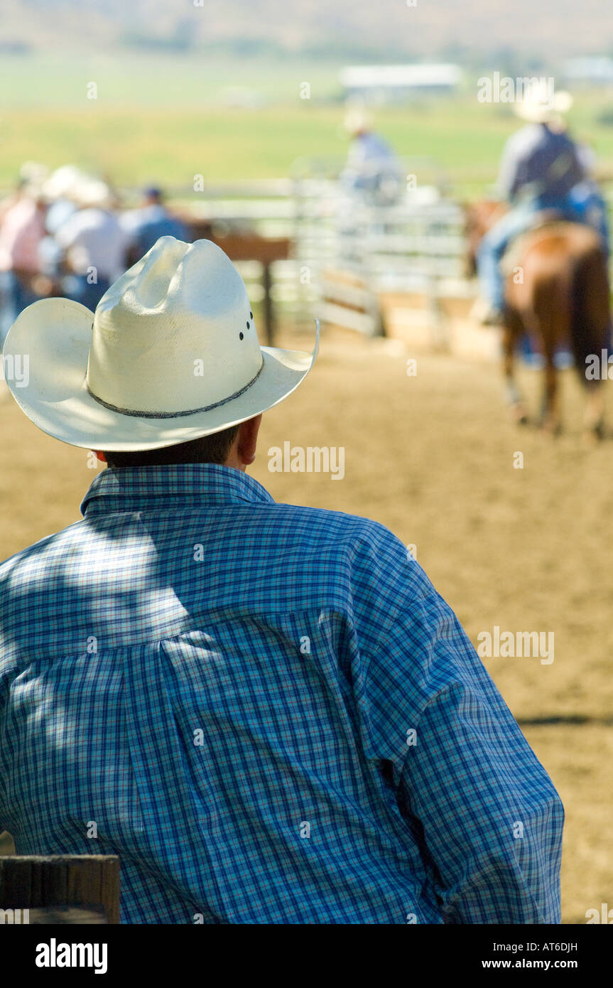 Ein Tag auf der Ranch. Ein Cowboy, der im Schatten steht, trägt einen weißen Hut im westlichen Stil und beobachtet Männer machen sich bereit für den Rodeo-Wettbewerb in der Nähe von Ellensburg, WA USA Stockfoto