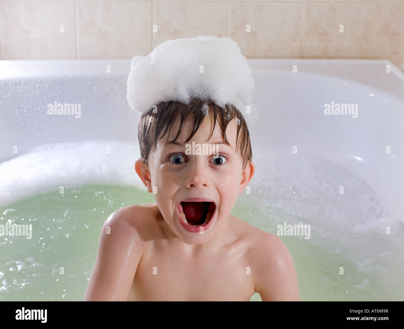 Kind mit lustig überraschten Blick in Wanne mit Luftblasen auf Kopf. Schaumbad. Stockfoto