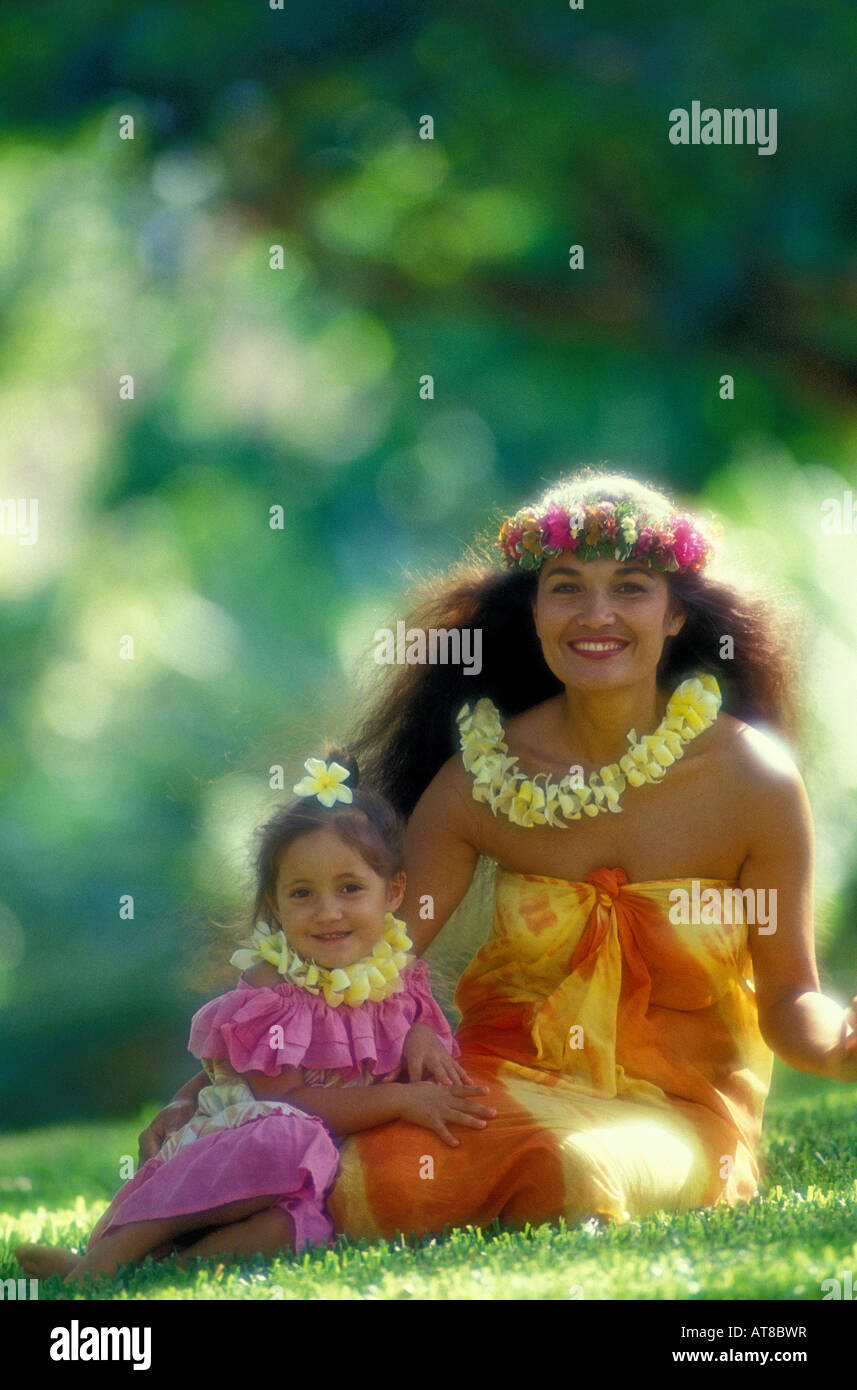 schöne polynesischen Frau mit ihrer Tochter in bunten aloha tragen und tragen Plumeria und Haku Leis, sitzen zusammen auf der Stockfoto