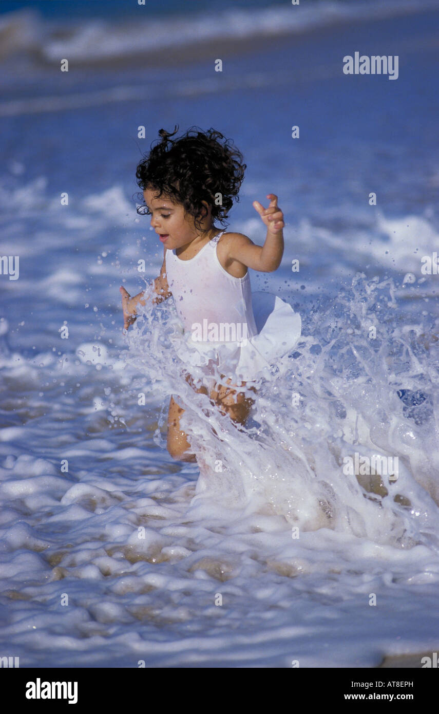 Ein junges Mädchen läuft durch die Wellen an der Küste von einem Strand auf der Insel Oahu. Stockfoto