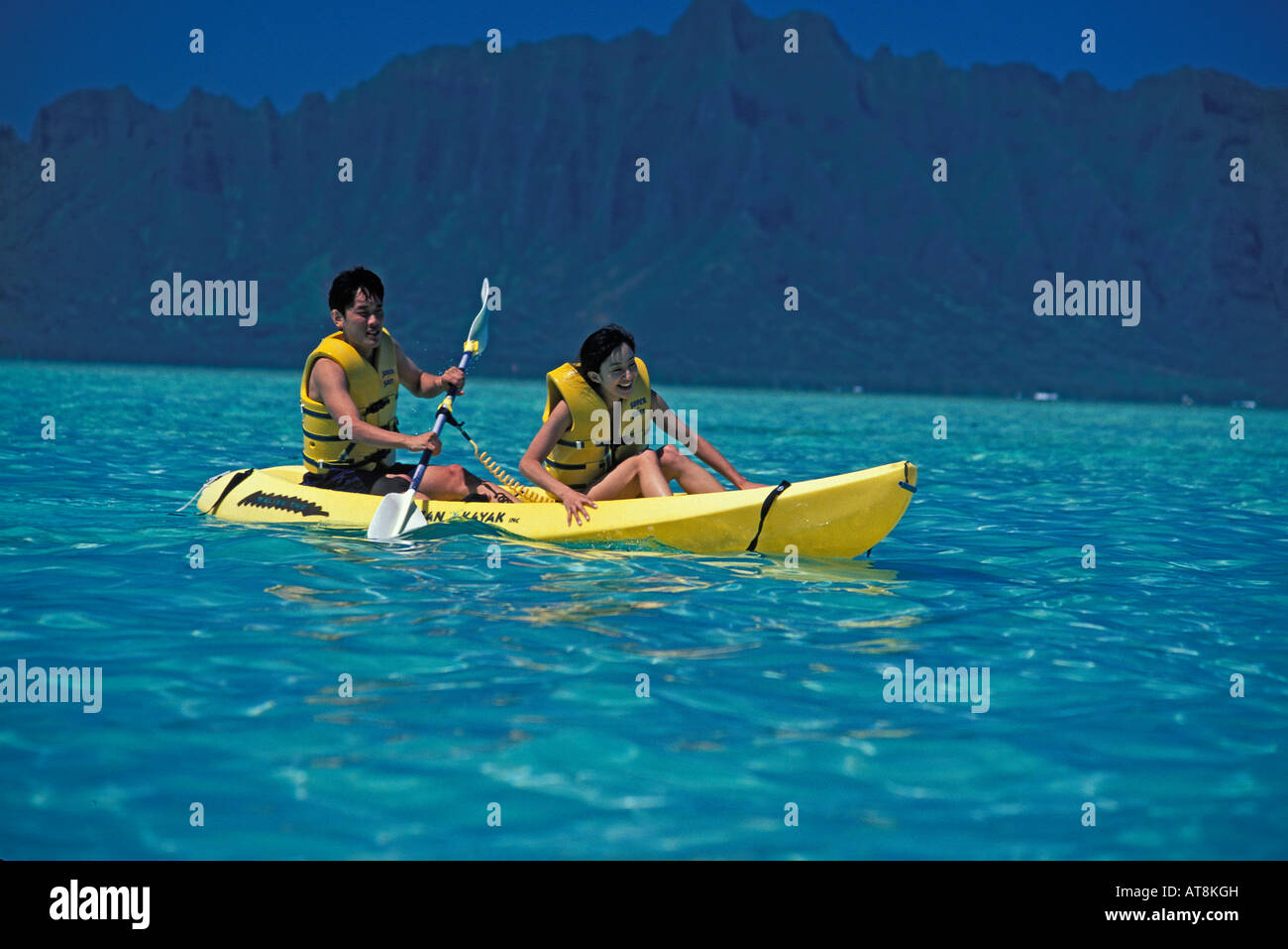 Japanisches Paar Paddiling gelben Kajak im türkisblauen Meer, Ahu o Laka, Kaneohe Bay, aus der Insel Oahu Stockfoto