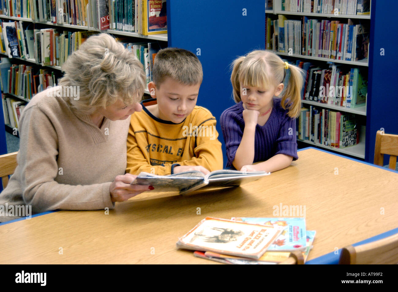 Mutter hilft, 9-jähriger Junge und 7 Jahre alten Mädchen mit Lesung in einer öffentlichen Bibliothek Stockfoto