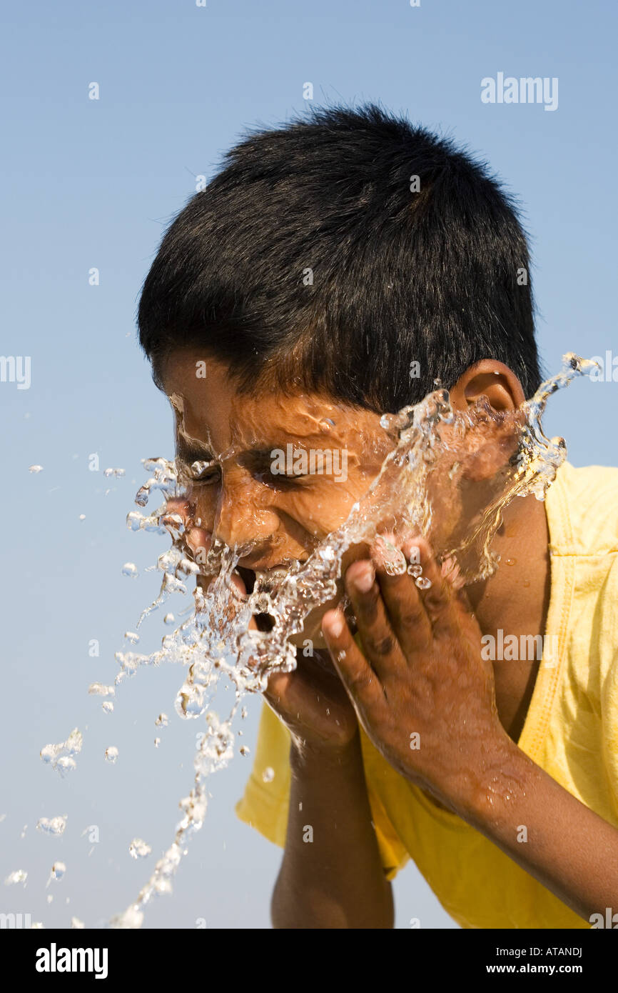 Indianerjunge Spritzwasser auf seinem Gesicht vor einem blauen Himmel. Indien Stockfoto