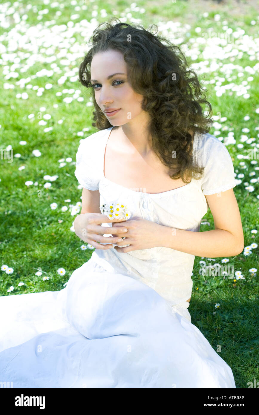Junge Frau sitzt auf dem Boden, mit Blumen, Blick seitwärts in die Kamera Stockfoto