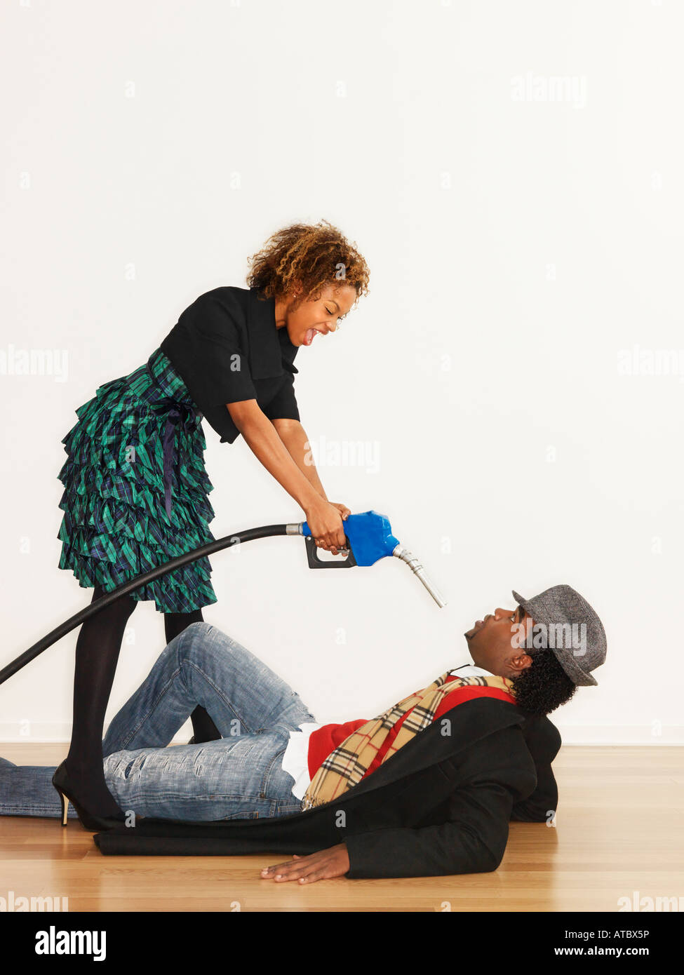 Mann am Boden mit böse Frau, die über ihn Benzin-Pumpe-Düse auf ihn zeigt, wie eine Waffe Stockfoto
