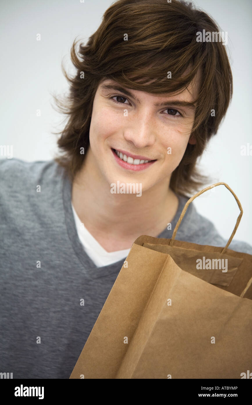 Junger Mann hält Einkaufstasche, lächelnd in die Kamera, Porträt Stockfoto