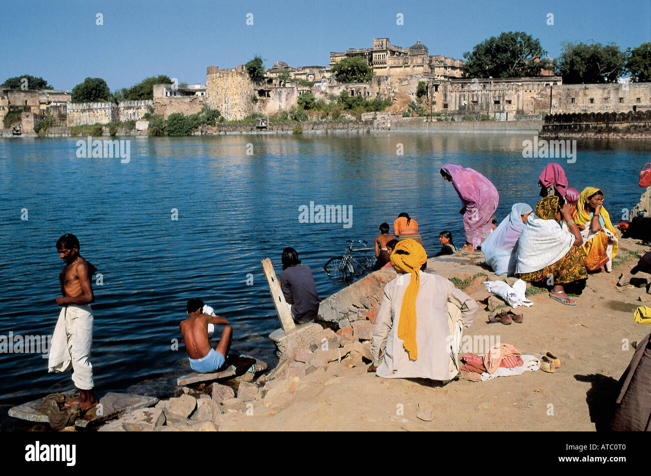 Menschen vor Ort sammeln neben den stillen Wassern des Chambal River, der durch die Kota Barrage gesteuert wird und ihre täglichen Aufgaben waschen oder einfach ein erfrischendes Bad zu genießen, während im Hintergrund eine stattliche Gebäude gesehen werden kann Stockfoto