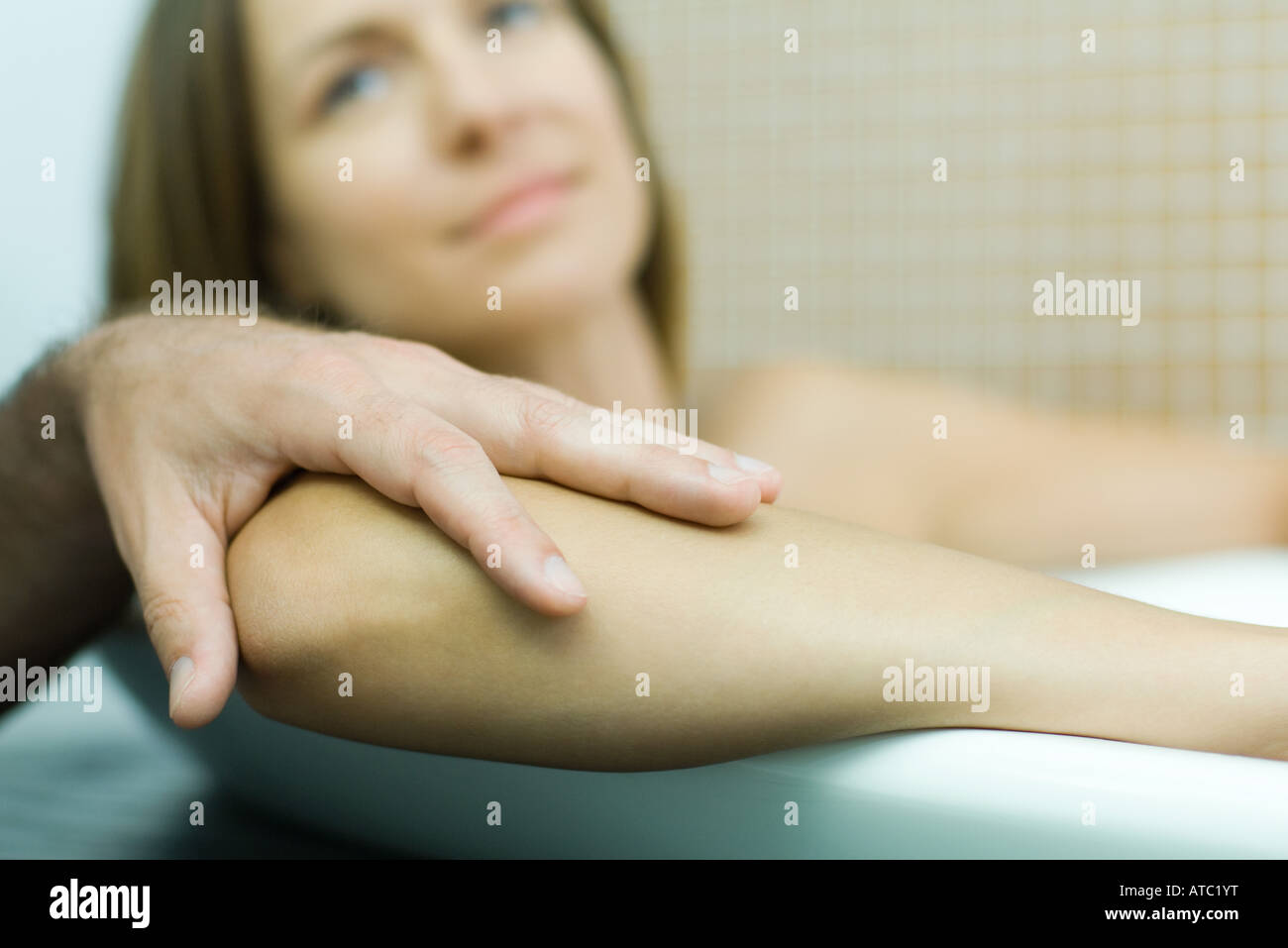 Frau in der Badewanne mit Hand des Mannes auf dem Ellenbogen, Fokus auf Vordergrund, beschnitten Ansicht Stockfoto