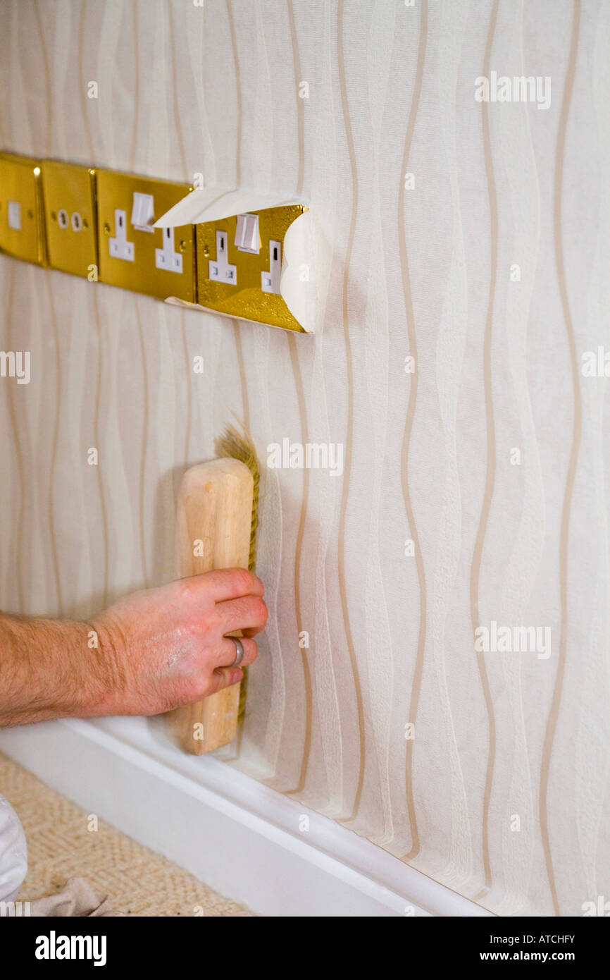 Person hängenden Tapete mit Dekorateur s Papier Pinsel hängen an Wand glätten runden Steckdosen. England-UK-Großbritannien Stockfoto