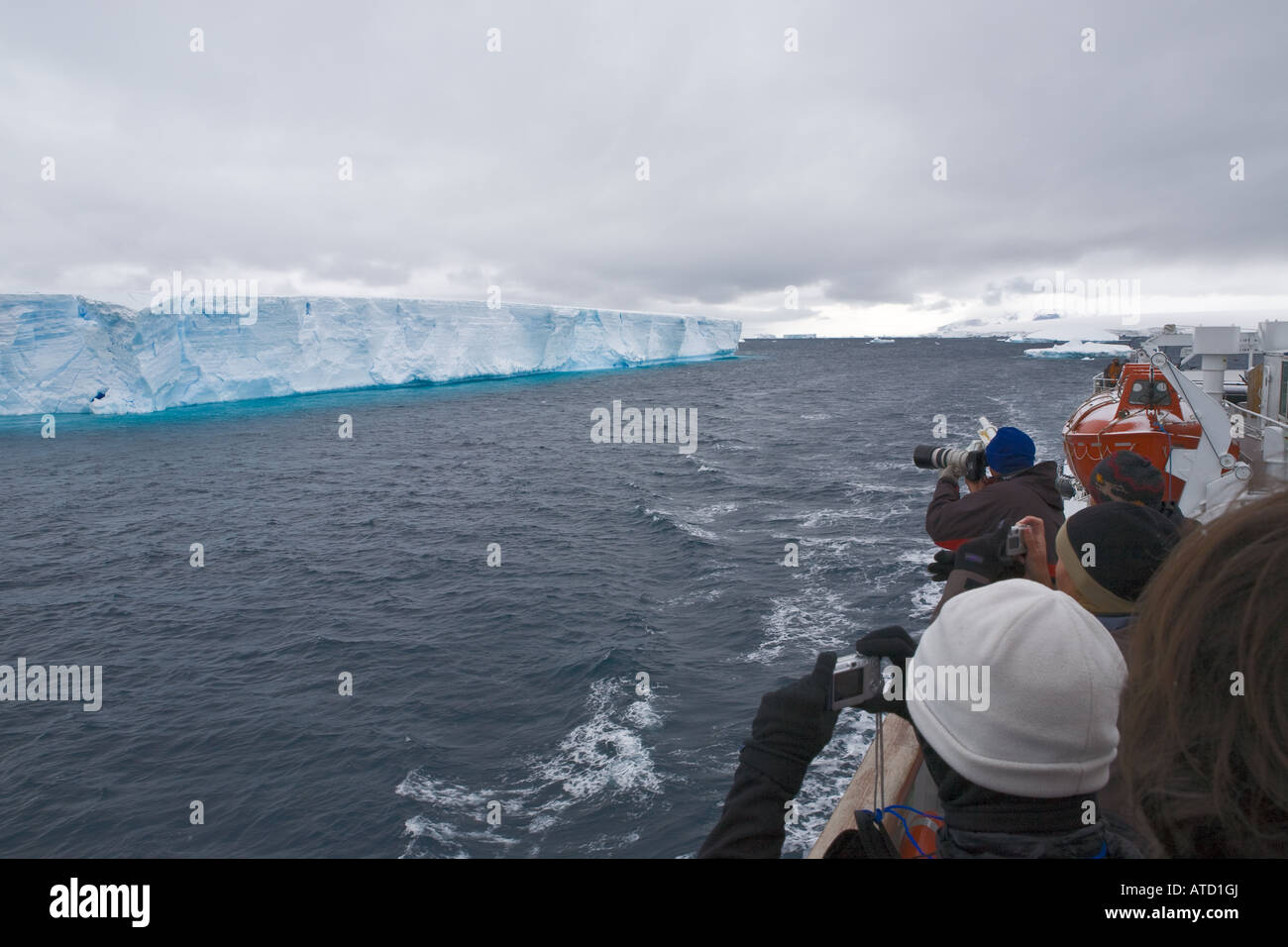 Gesichtslose Touristen fotografieren riesigen Eisberg mit blauen Reflexionen von Schiff im antarktischen Meere Stockfoto