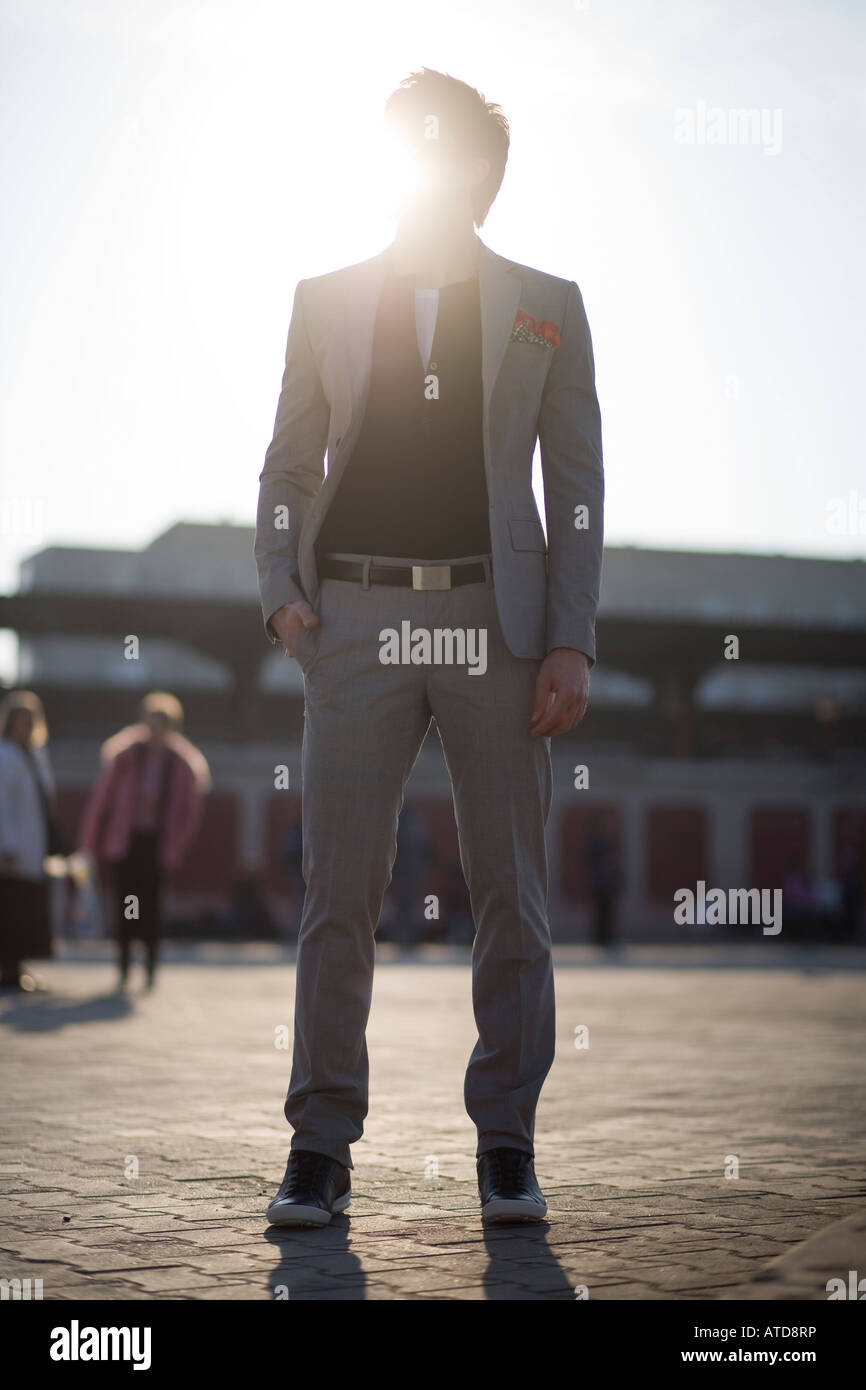 junger Mann gekleidet in Anzug stehend in der Mitte einer Straße mit seiner Hand in der Tasche Stockfoto