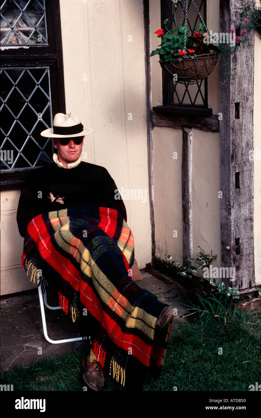 Mann trägt einen Panamahut-Sittiing auf einem Garten Stuhl vor einem Landhaus mit einem Tartan Teppich über seine Beine Stockfoto