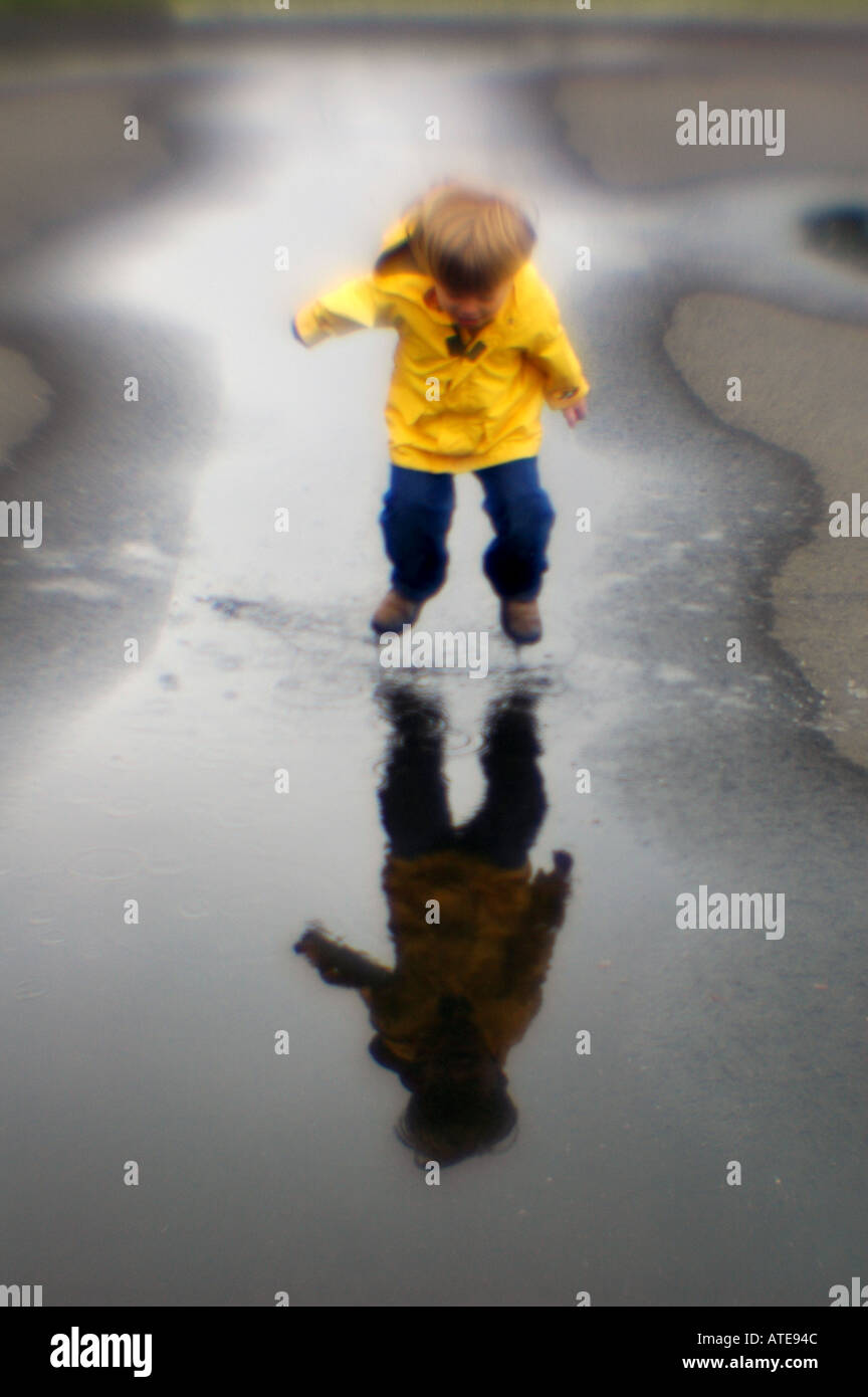 Kleiner Junge spielt in Pfütze Wasser gelbe Jacke im Regen spielen Stockfoto