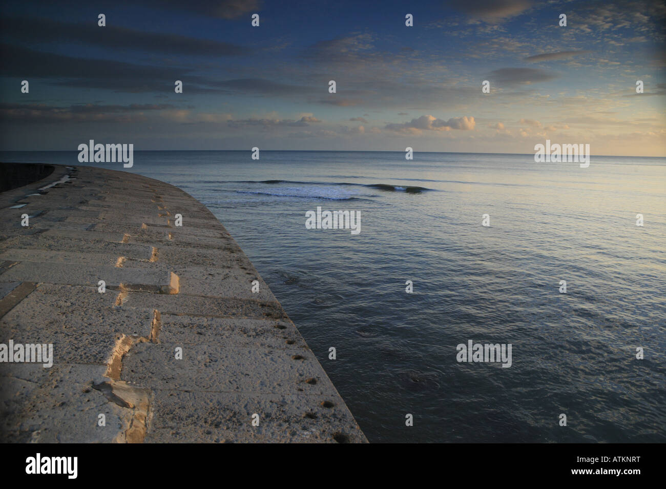 Seelandschaft mit Stein Hafen Wand im Vordergrund in der Morgendämmerung mit bunten Himmel aber weich und gedämpfte Töne Stockfoto