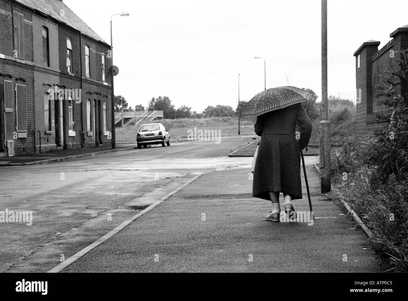 Ältere Frau, die zu Fuß in Regen im städtischen Umfeld Stockfoto