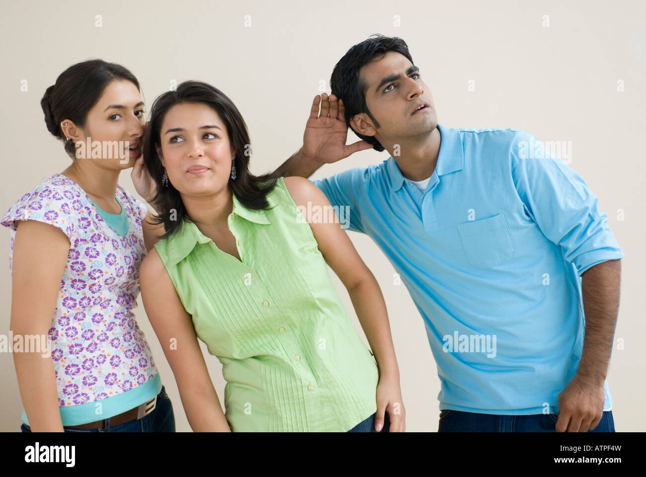 Porträt einer jungen Frau, Flüstern ins Ohr eine andere junge Frau und ein junger Mann versucht, sie zu hören Stockfoto
