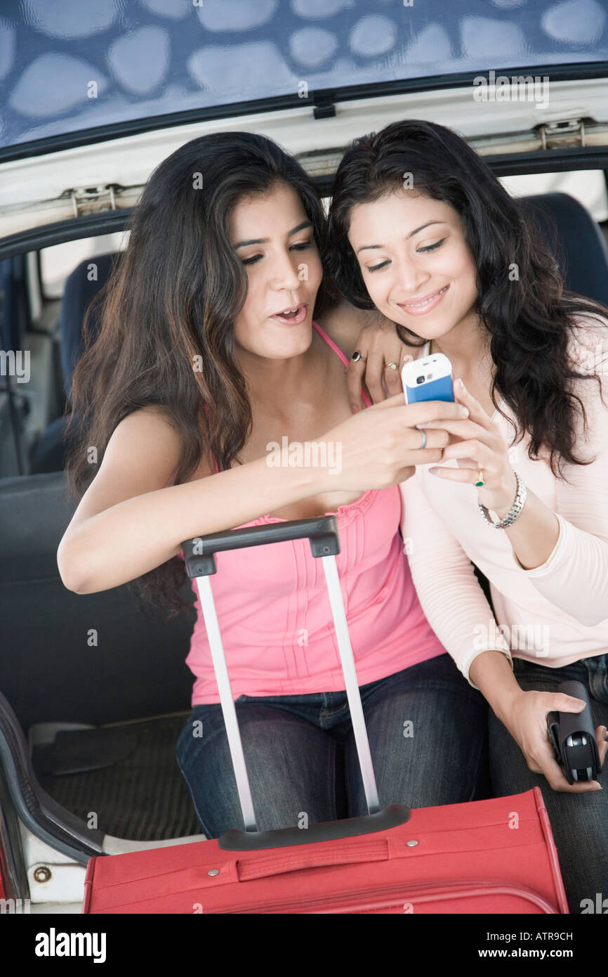Zwei junge Frauen in einem Kofferraum eines Autos sitzen und mit Blick auf ein Mobiltelefon Stockfoto