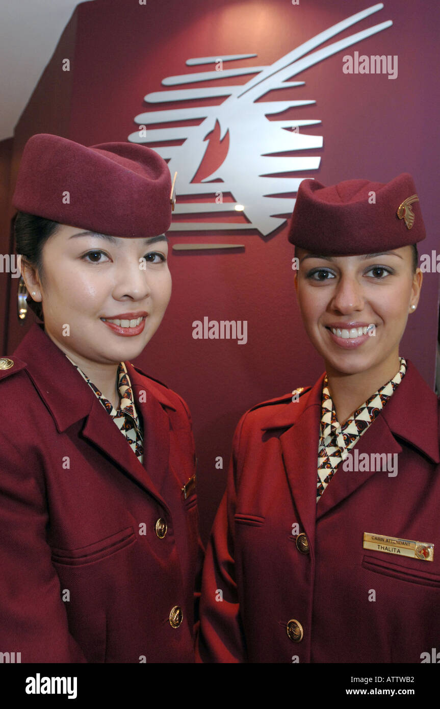 Flugbegleiterinnen in der Qatar Airways einheitliche und Logo hinter Ihnen Stockfoto