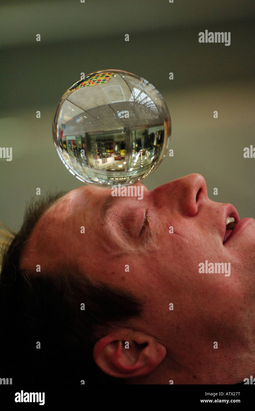 ein Illusionist Straßenkünstler mit Blick in balancieren auf seiner Stirn eine Kristall-Glaskugel durchführen in einem Einkaufszentrum Stockfoto